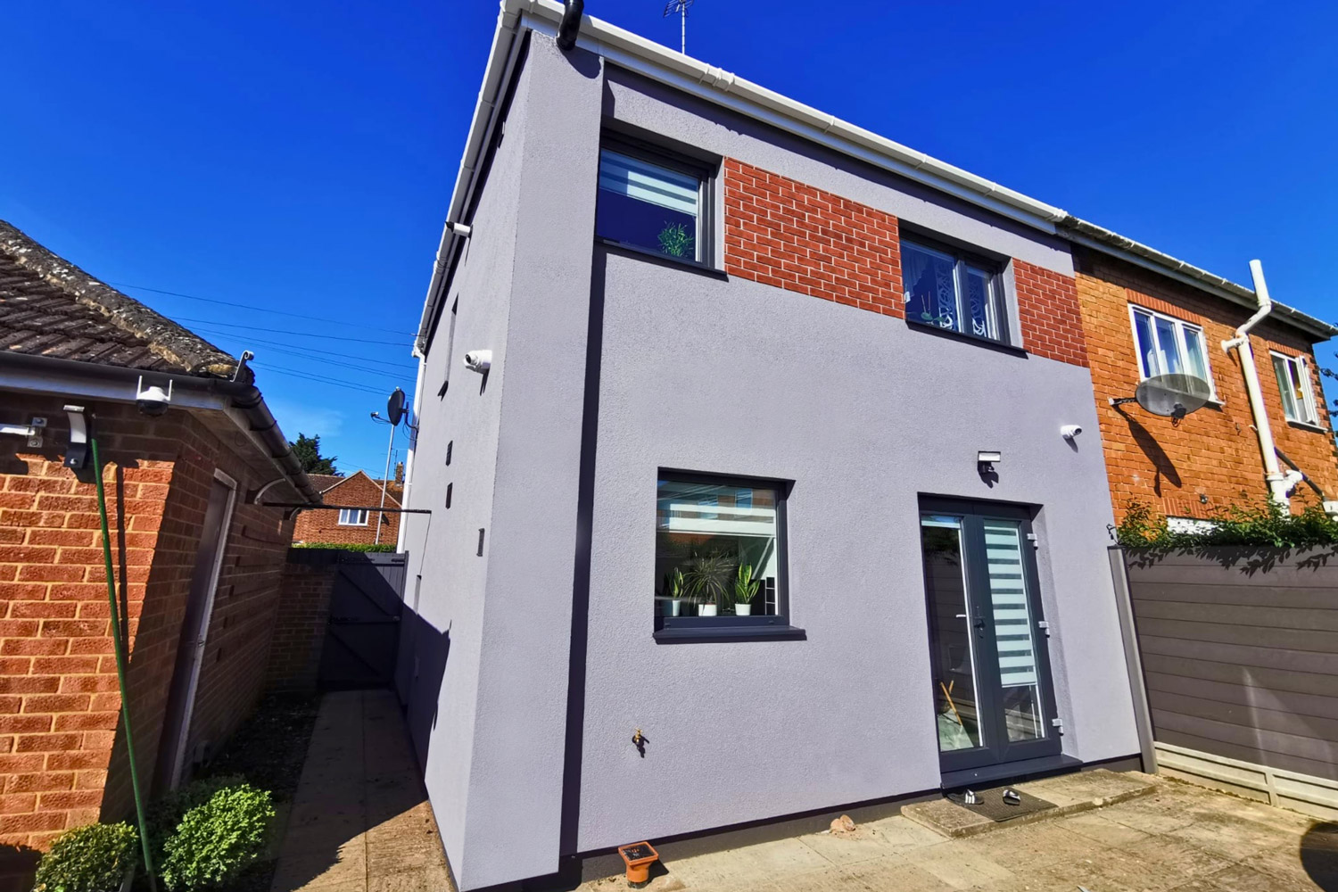 A modernised UK property featuring a highly durable light grey exterior render, perfectly combined with original red brickwork on the upper floor.